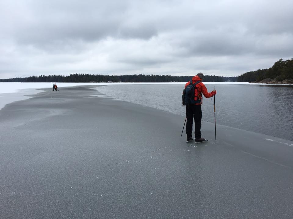 Skater checking the ice thickness with a pole, next to open water.